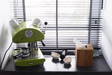 Retro style coffee-maker, a splash of color on the black windowsills next to black wooden blinds.